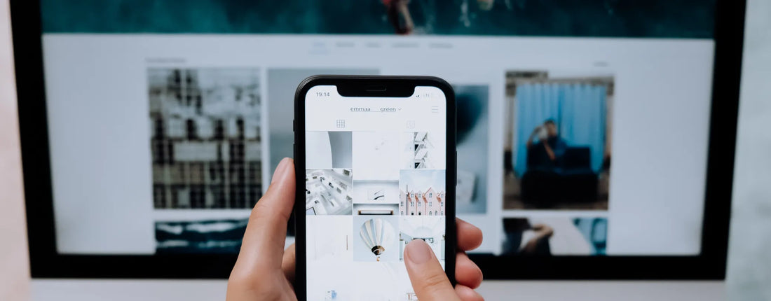 a hand holding a mobile phone in the foreground while a social media app is open on a computer in the background reposted by Pixel Profiles